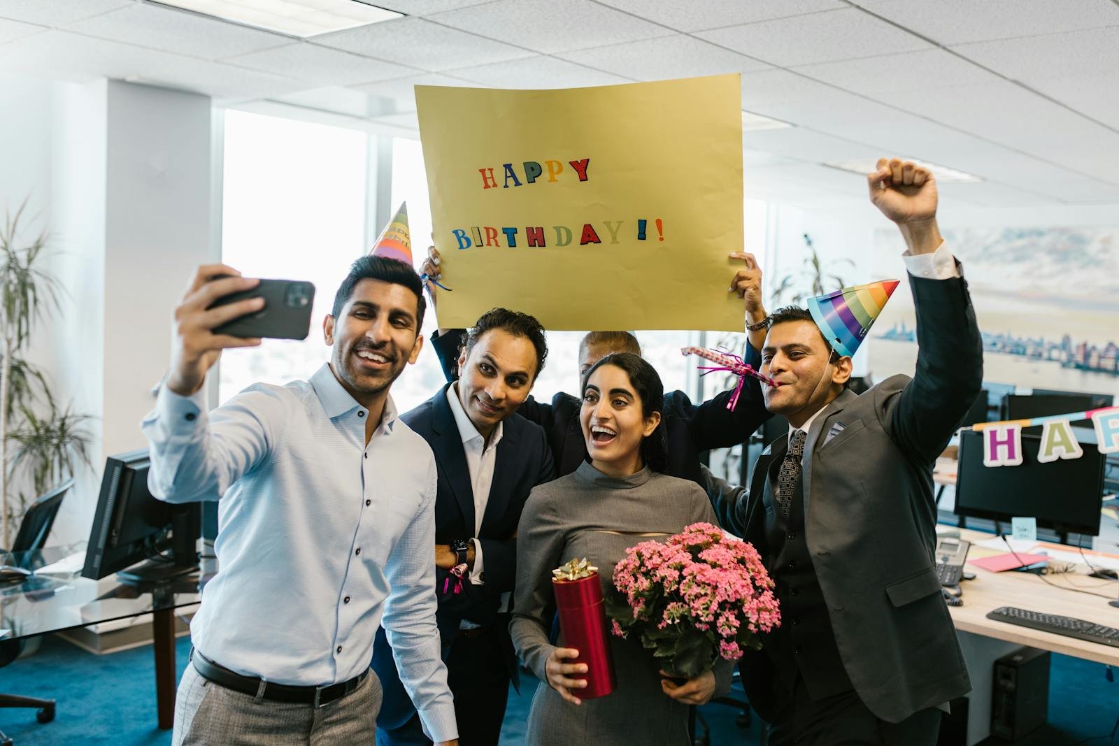 Group of colleagues celebrating a birthday in the office with gifts and a selfie.