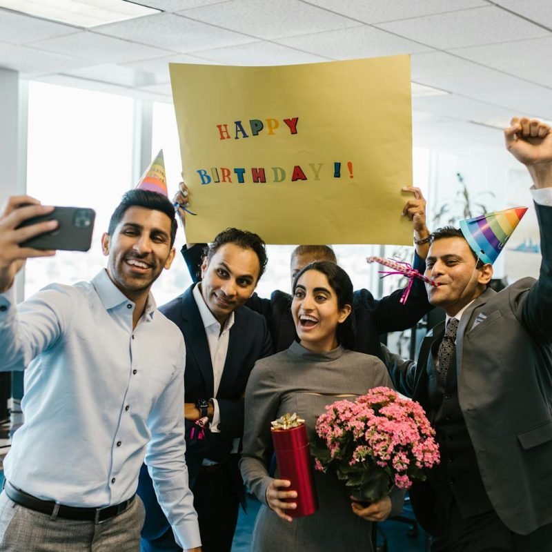 Group of colleagues celebrating a birthday in the office with gifts and a selfie.